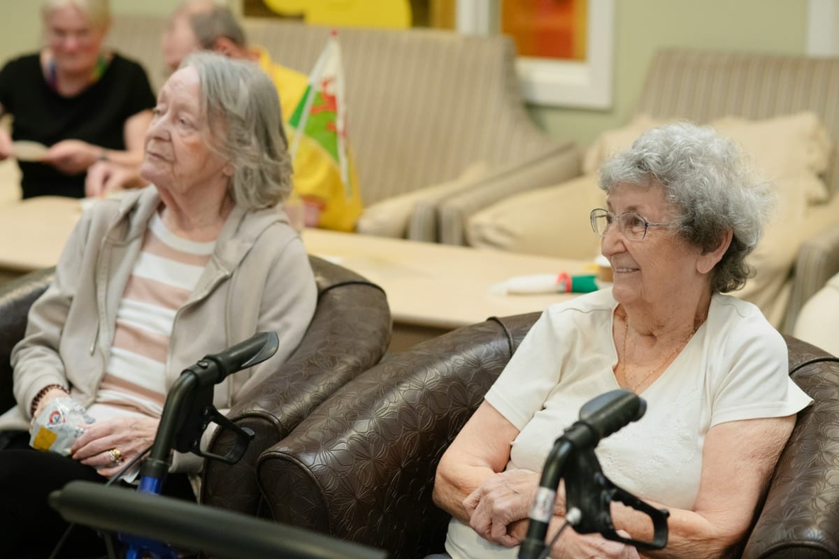 Two senior women enjoying each other's company in a warm, comfortable common room
